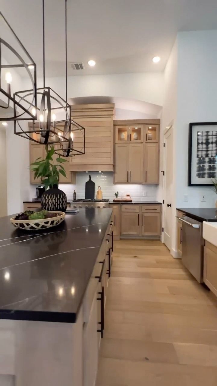 Cucina moderna con piano di lavoro scuro, mobili in legno e grandi lampade a soffitto.