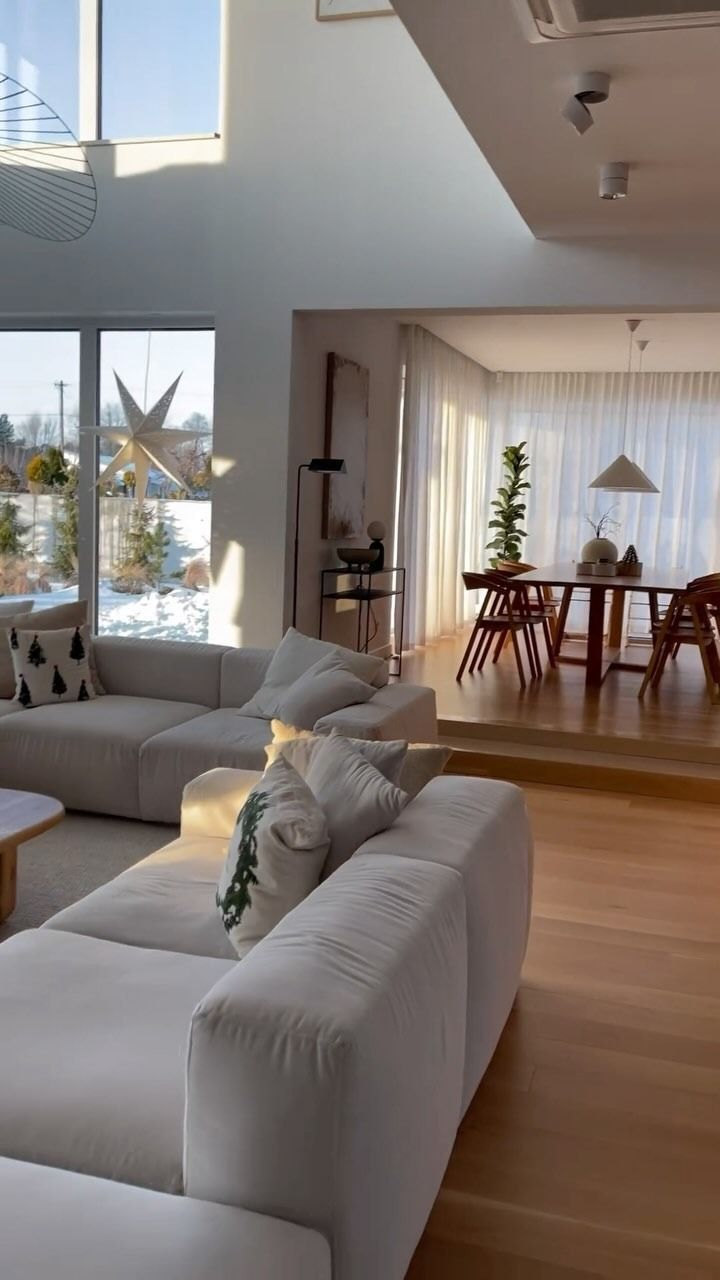 Soggiorno luminoso e spazioso con ampie finestre, divano componibile color crema e zona pranzo rialzata.