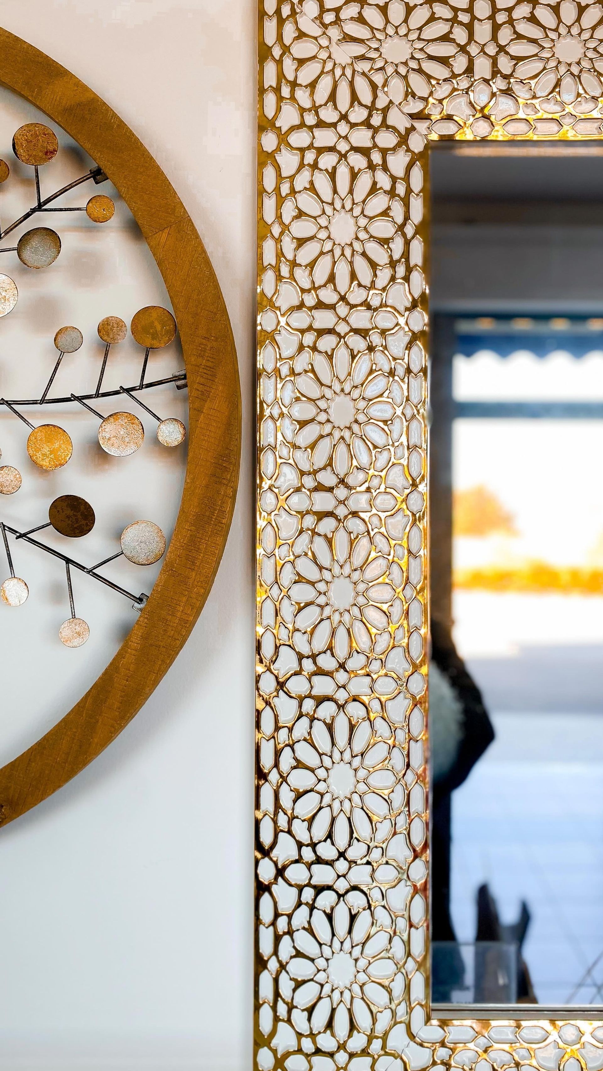 Specchio decorato con cornice dorata decorata accanto a un quadro circolare con dettagli dorati e argentati.