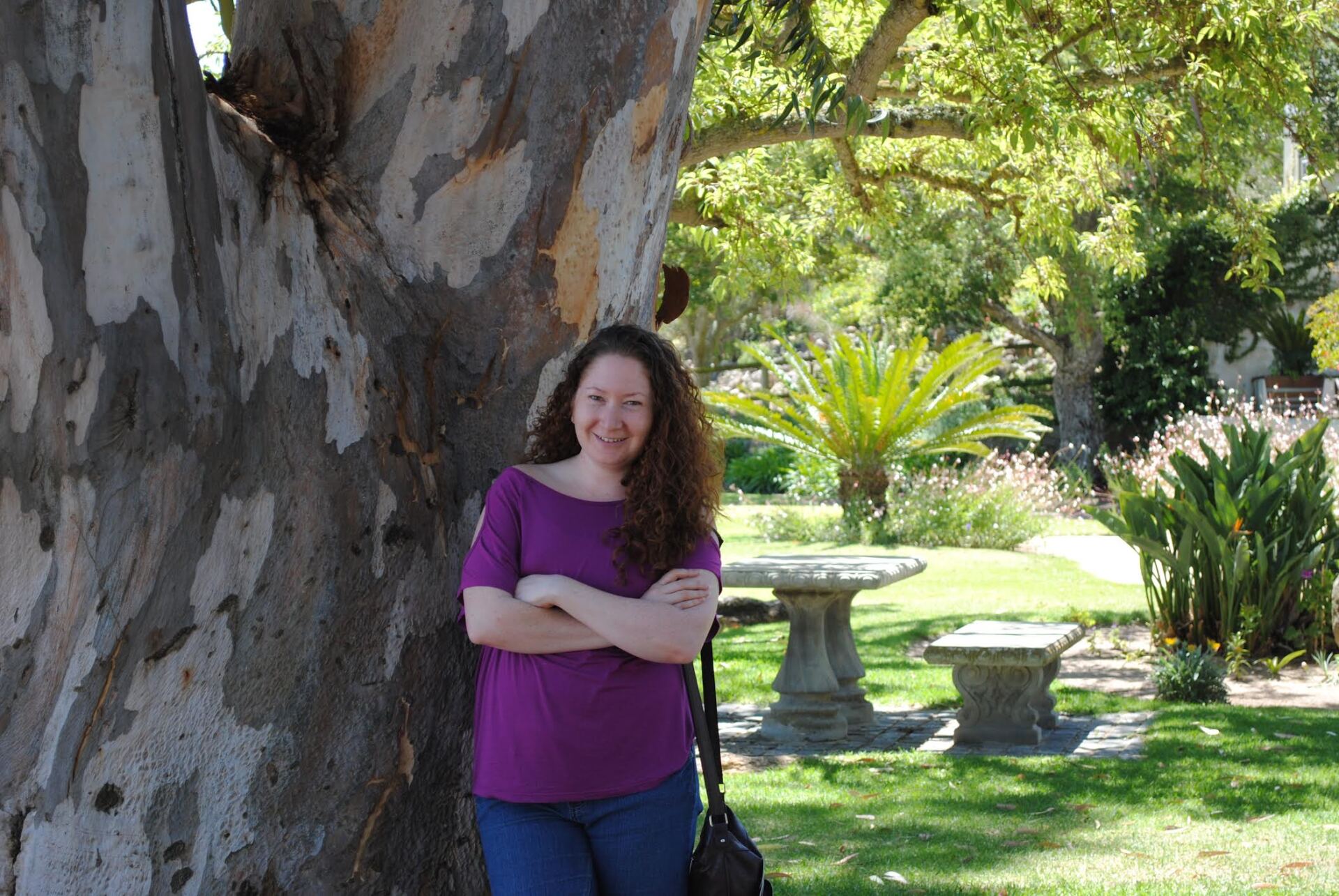 A woman in a purple shirt is standing next to a tree