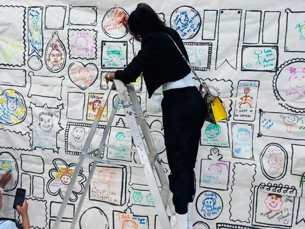A woman is standing on a ladder in front of a wall with drawings on it.