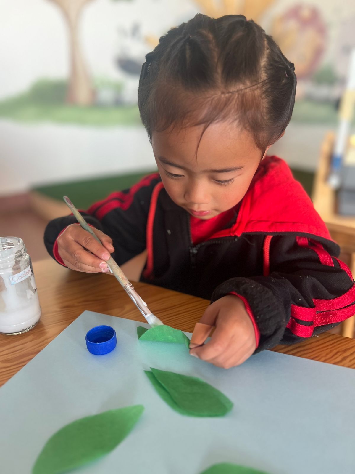 A little girl is painting green leaves on a piece of paper