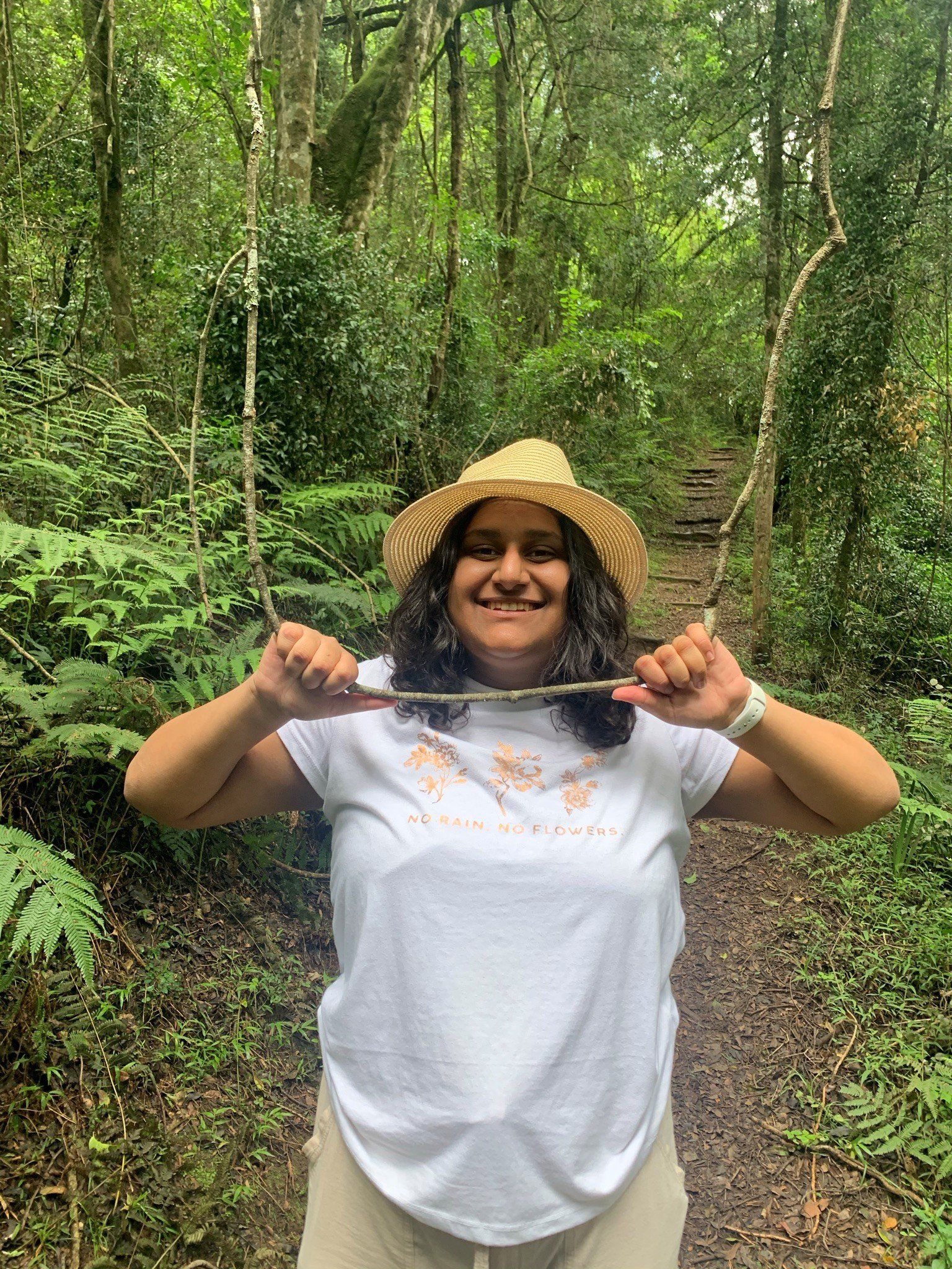 A woman in a hat is holding a stick in the woods.
