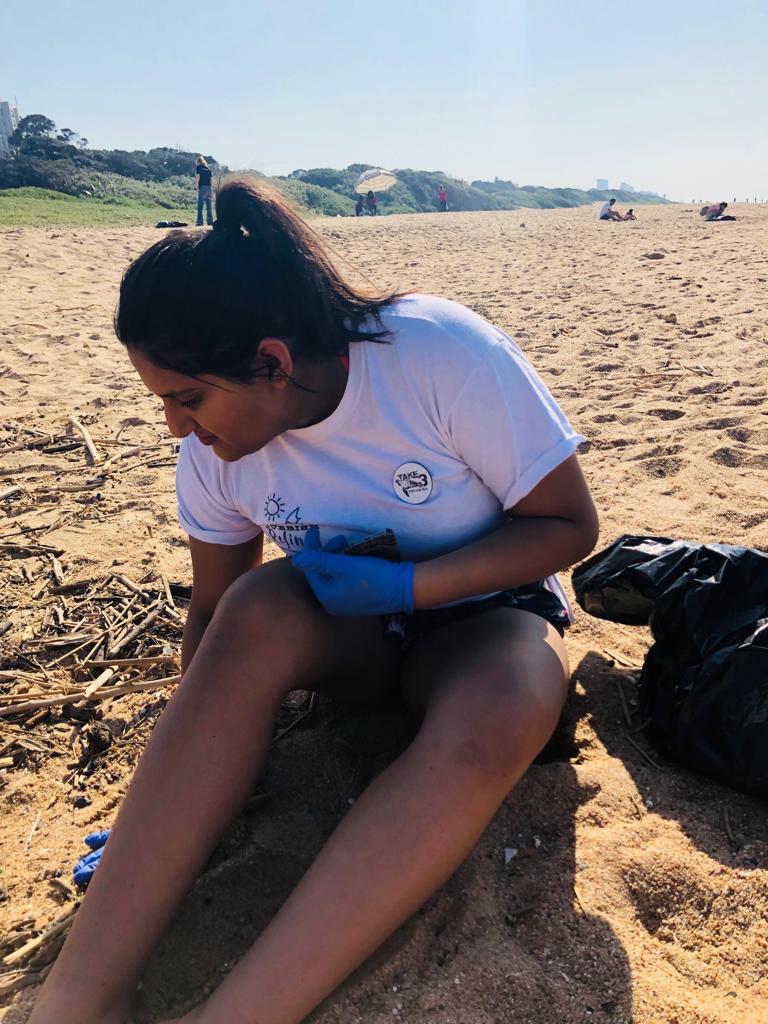A woman wearing blue gloves is sitting on a sandy beach.