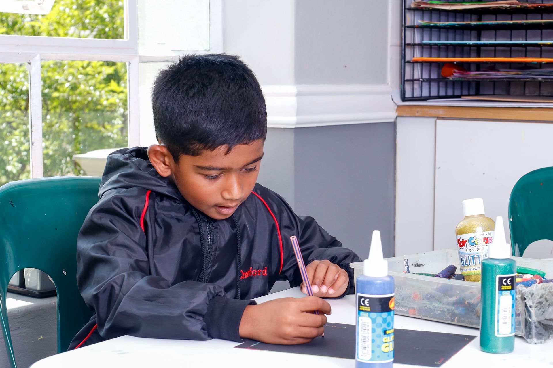 a young boy is sitting at a table painting with a brush .