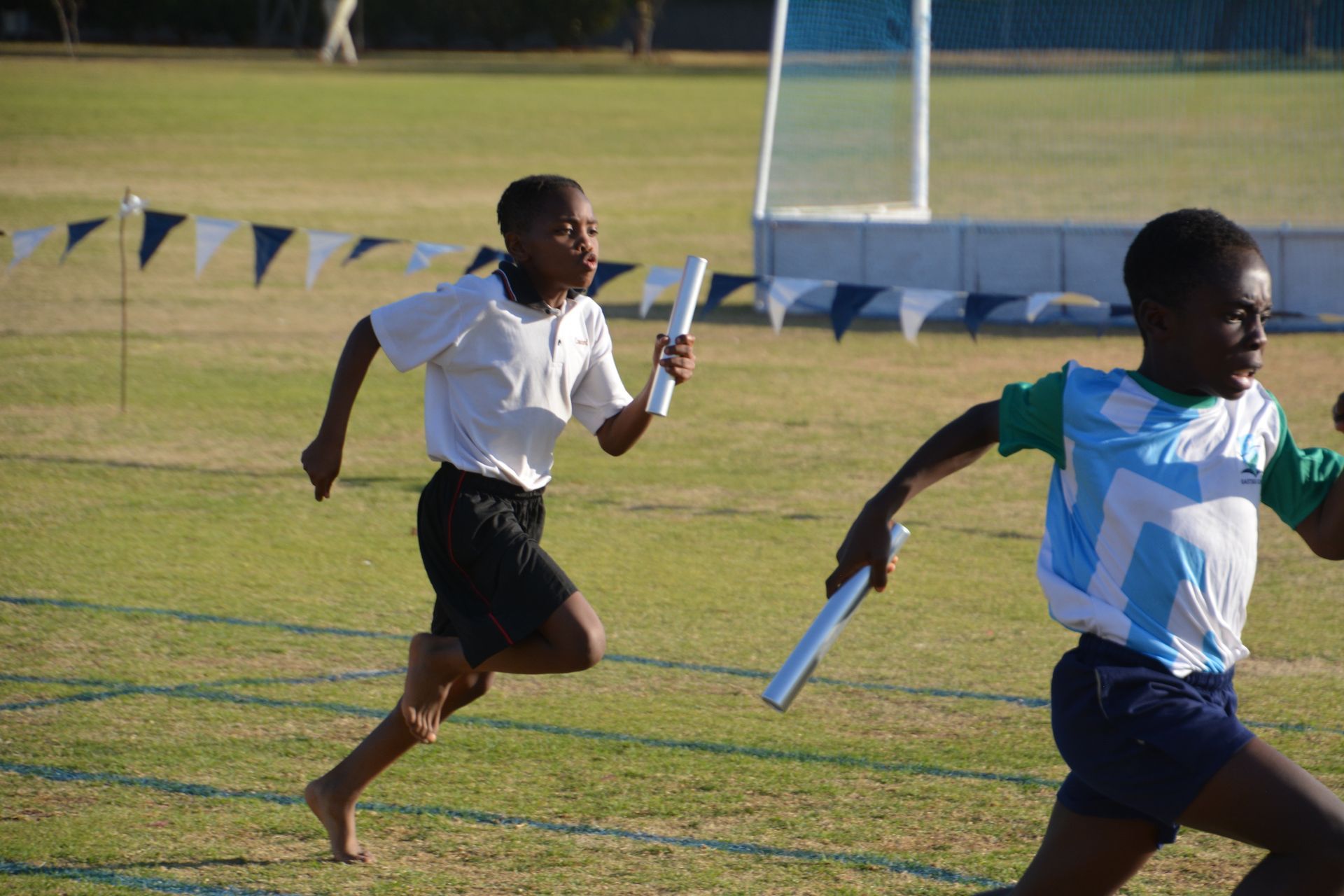 Two young boys are running a relay race on a field.