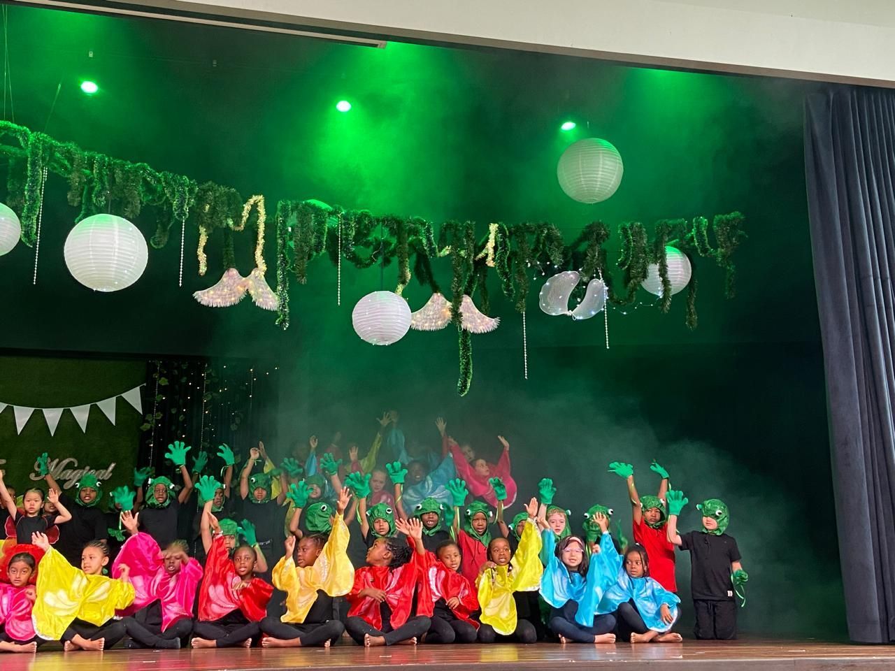 A group of children are dancing on a stage with green lights.