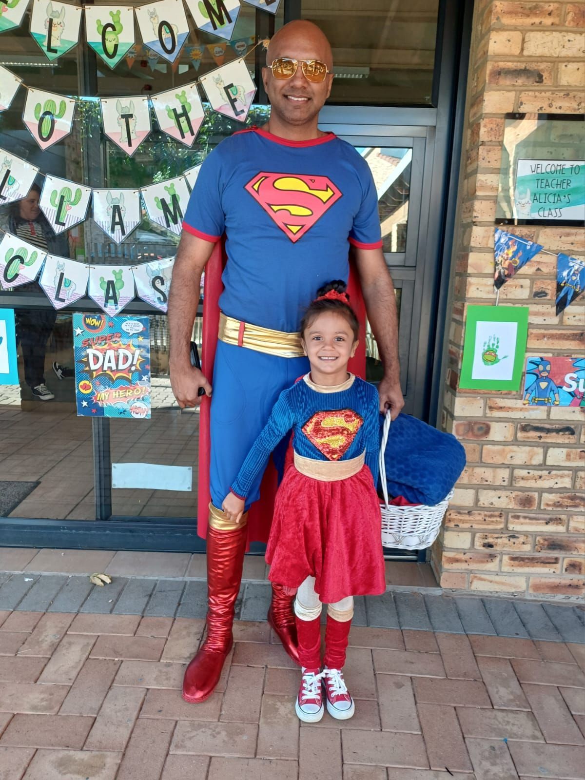 A man and a little girl dressed in superman costumes are standing next to each other.