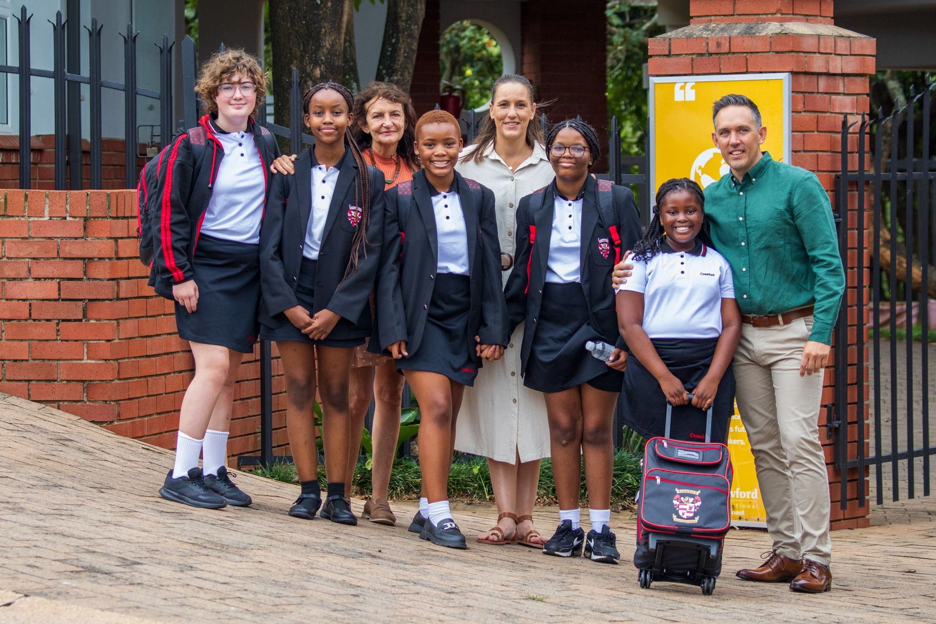 Group of students and adults posing by a brick gate. Students wear school uniforms.