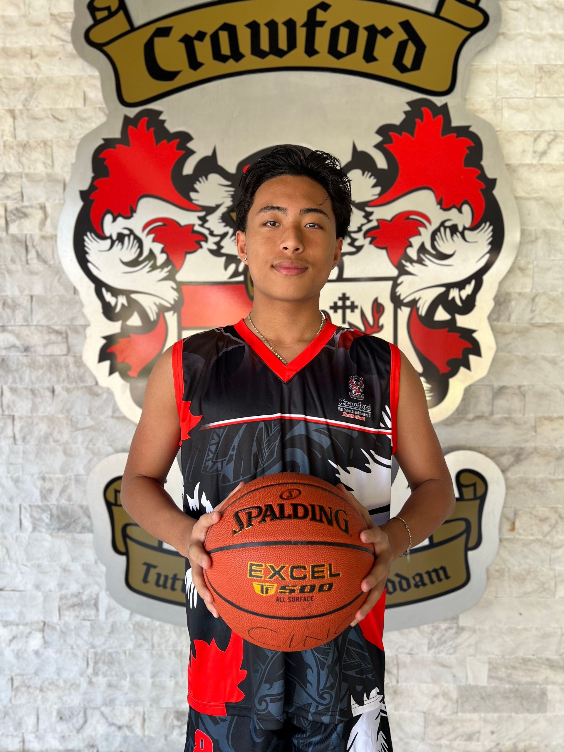 A young man holding a spalding basketball in front of a crawford crest