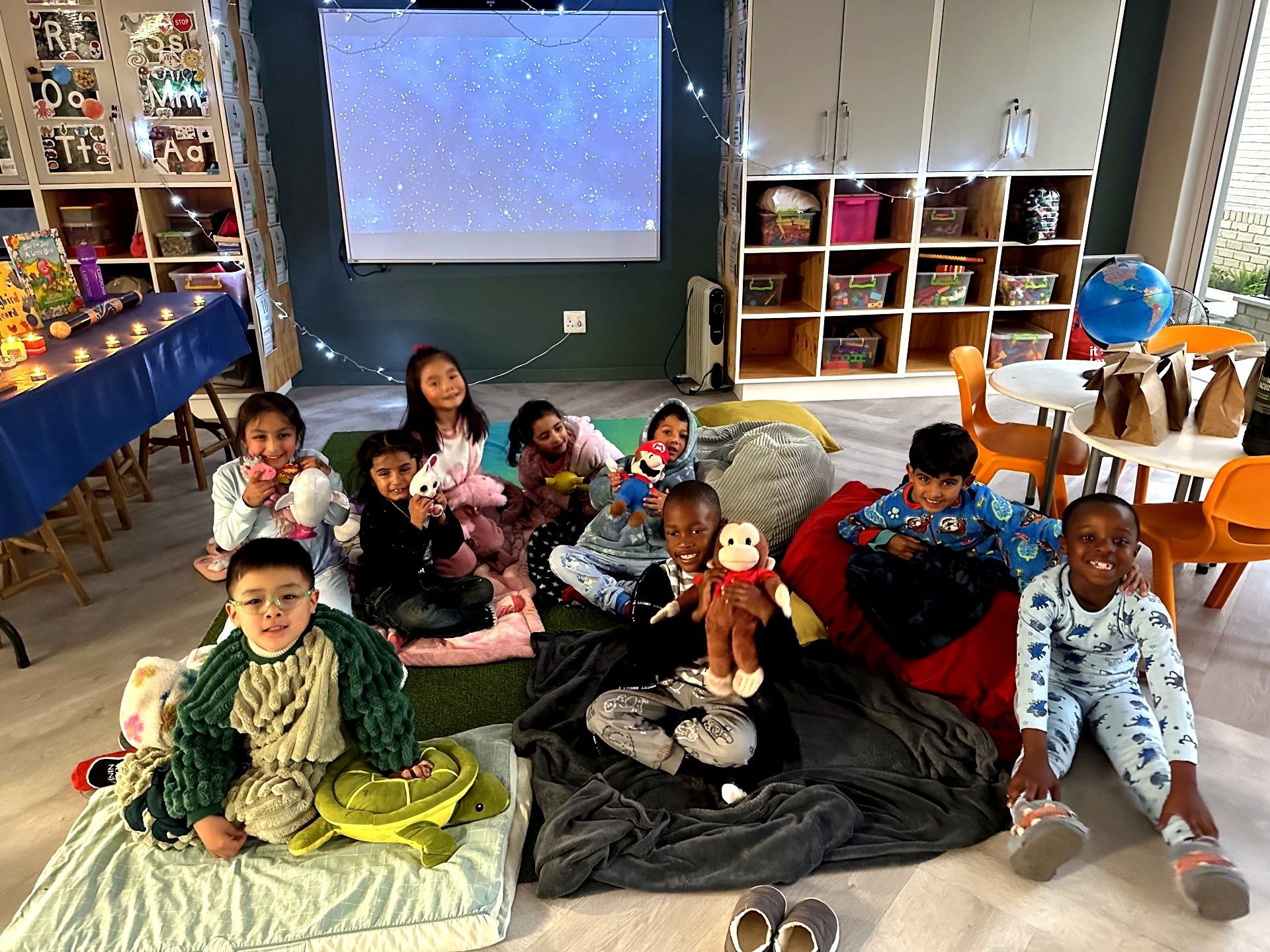 Children in pajamas smile at the camera during a slumber party in a classroom.