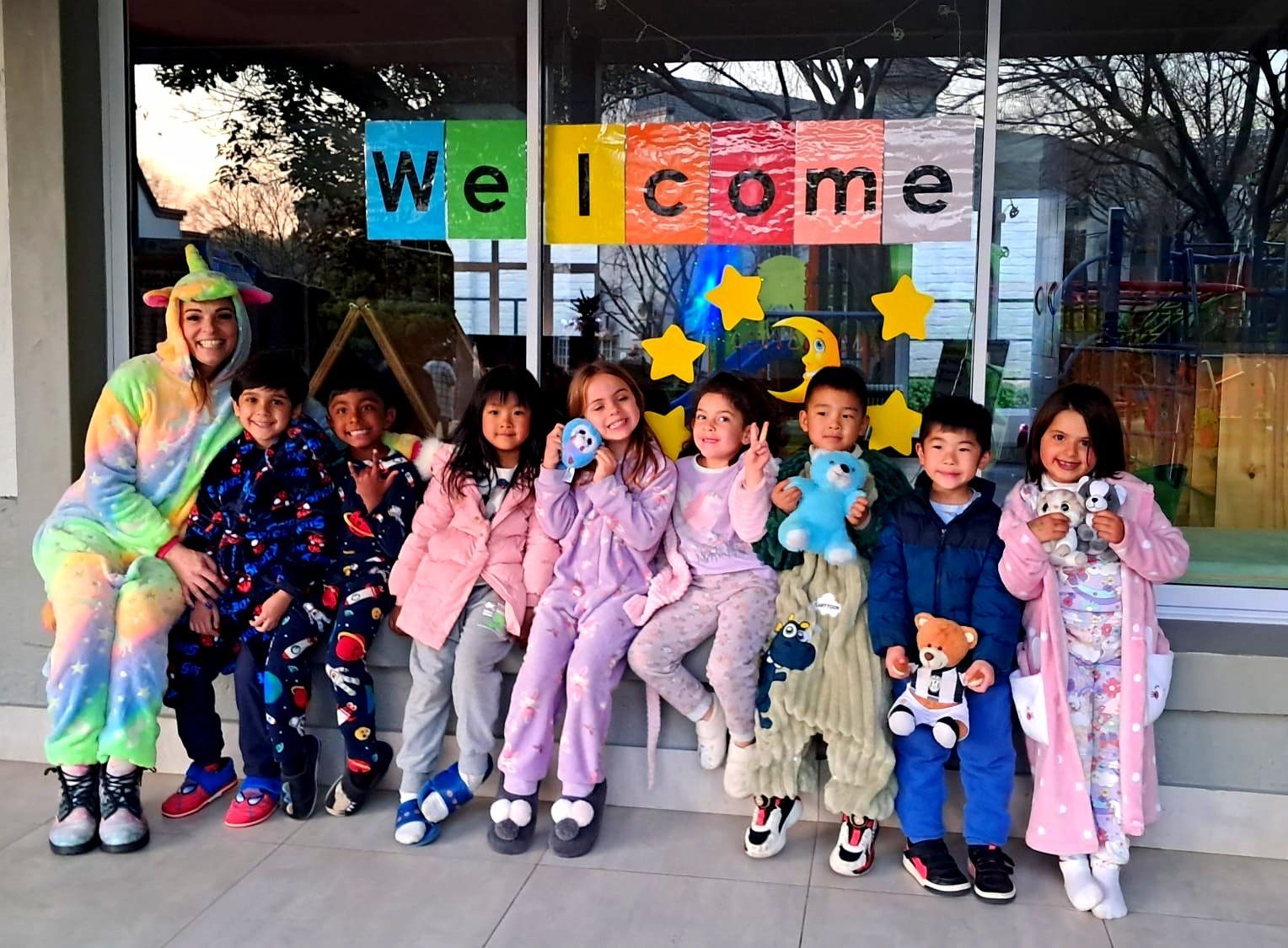 A group of children in pajamas, and a teacher, pose under a