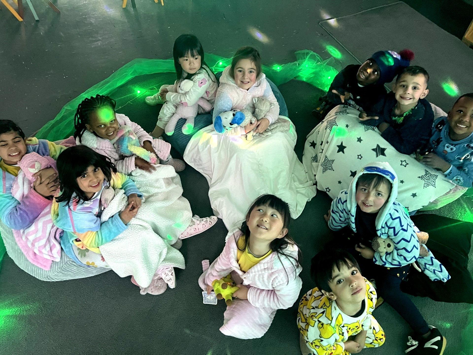 Children in pajamas sit together, illuminated by green light, possibly a slumber party.