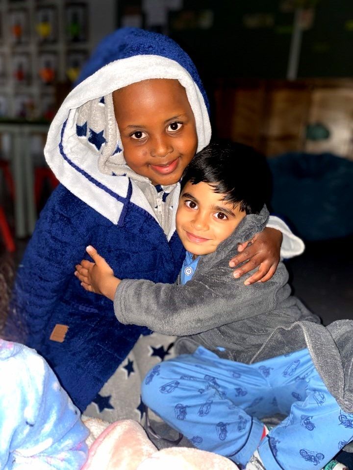 Two children in cozy blue and gray pajamas hug, smiling indoors.