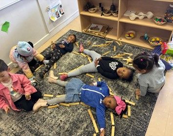 A group of children are laying on the floor playing with wooden sticks.
