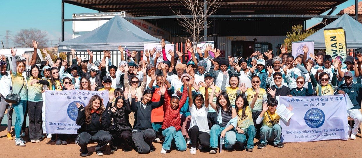 Large group of people gathered outdoors, raising hands. Holding banners, tents in background. Sunny day.
