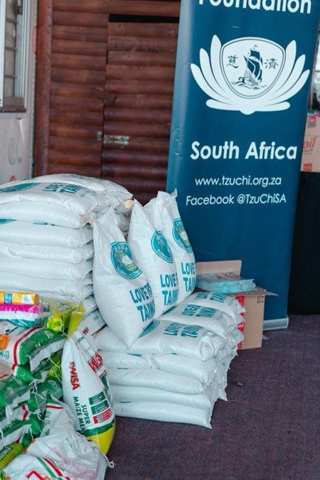 Bags of food donations stacked in front of a blue banner for a South Africa foundation.
