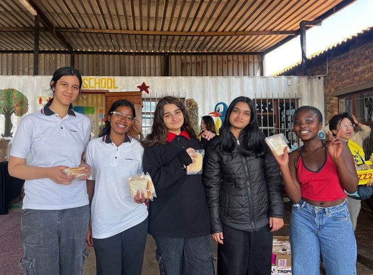 Five young people holding food smile near a building with