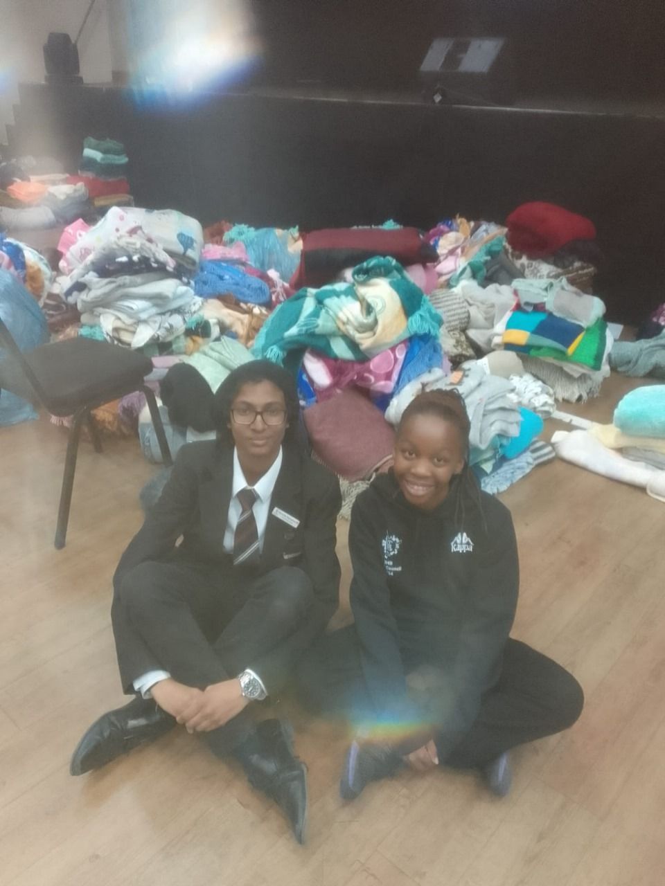 Two people are sitting on the floor in front of a pile of clothes