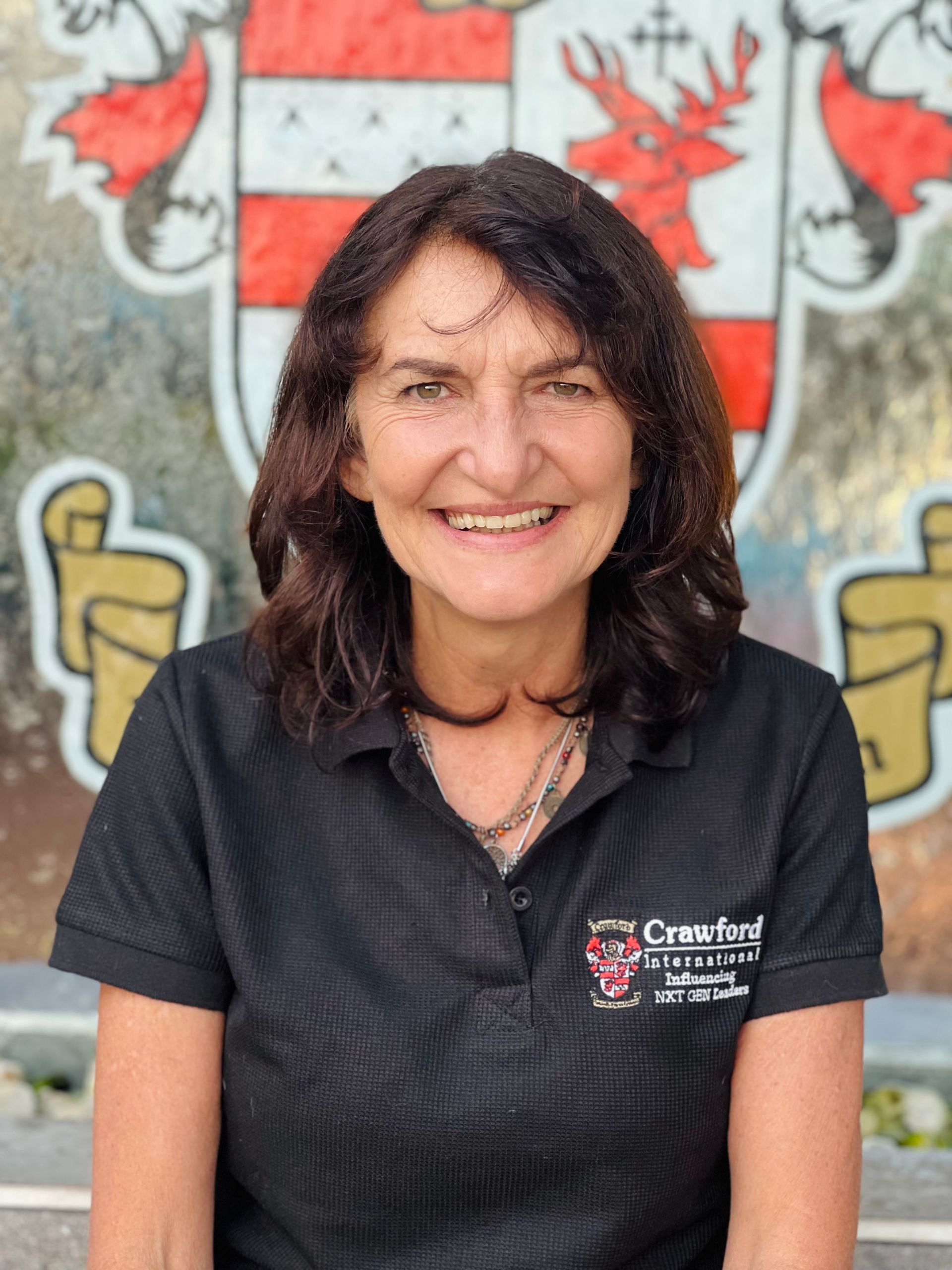 A woman in a black shirt is smiling in front of a coat of arms.