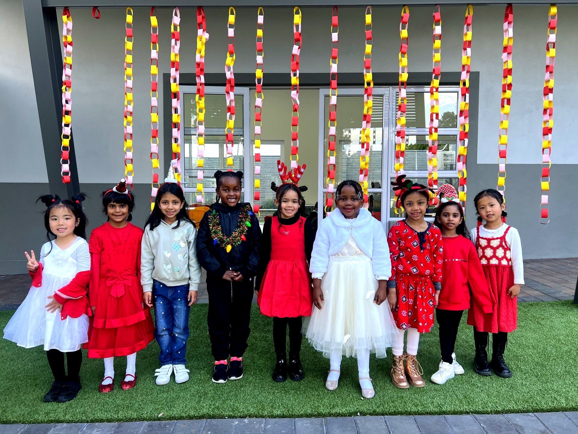 Children in red and white outfits pose in front of colorful paper chains.