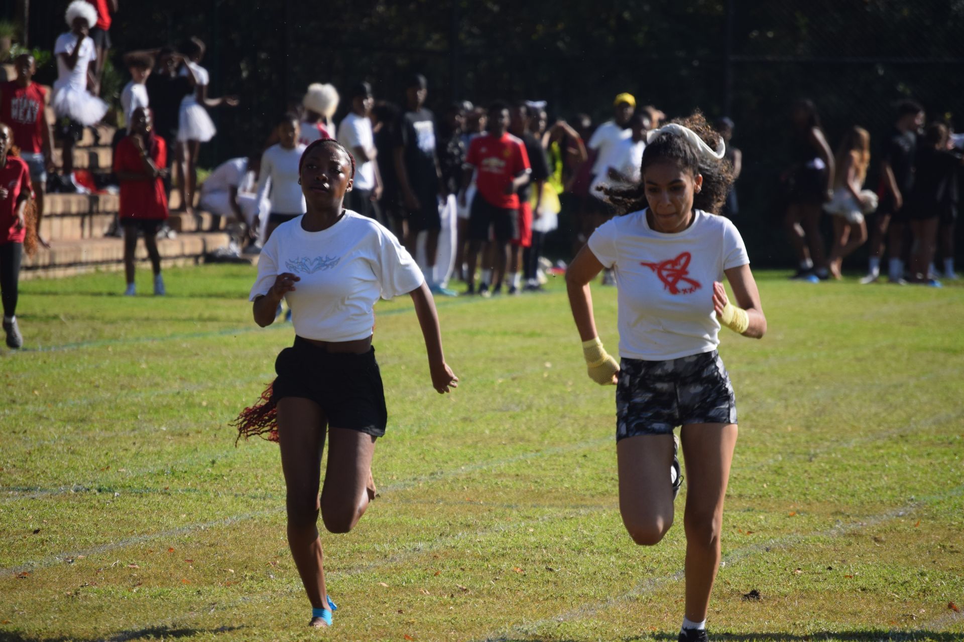 Two runners sprint across a grassy field; crowd in background.