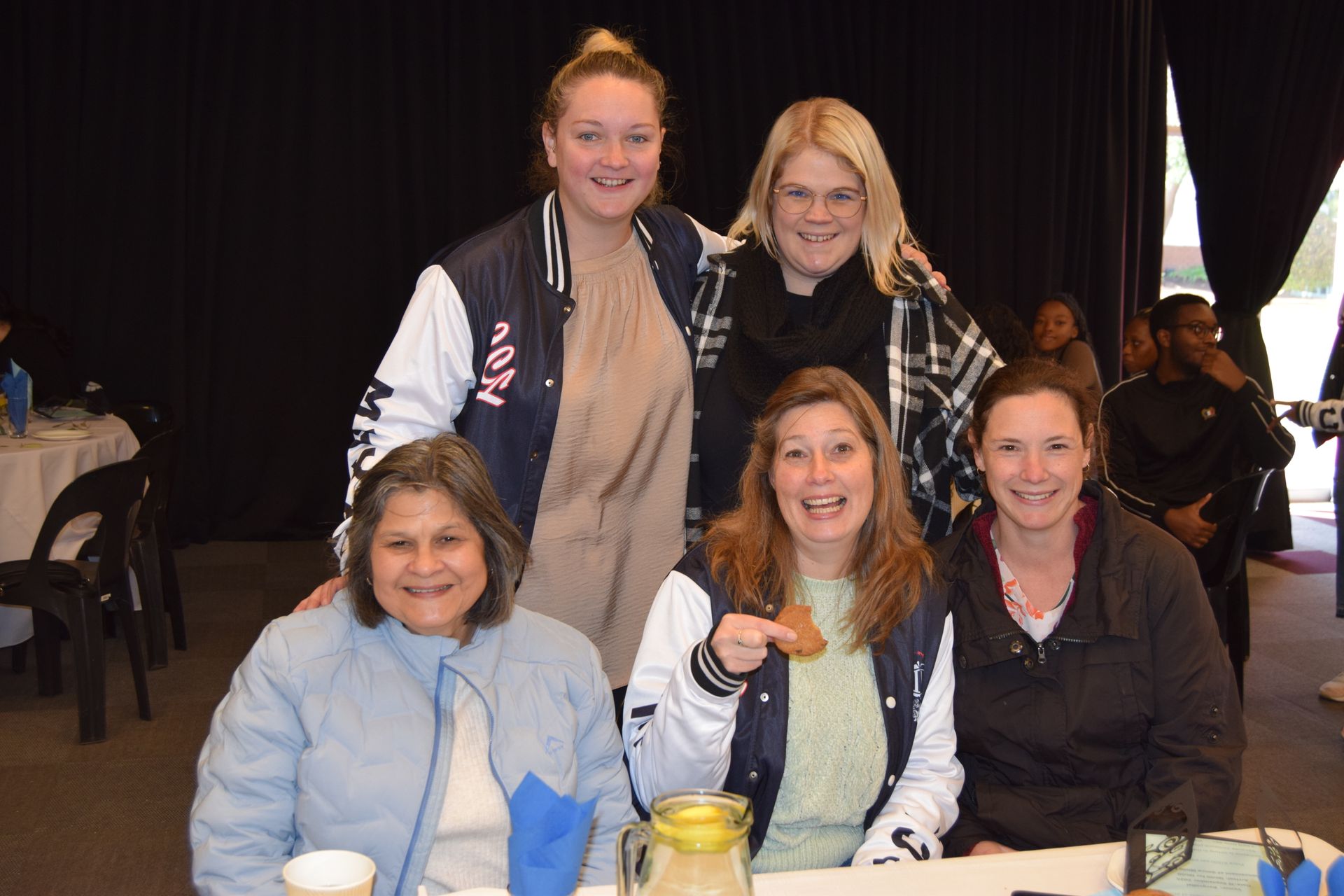 A group of women are posing for a picture while sitting at a table.