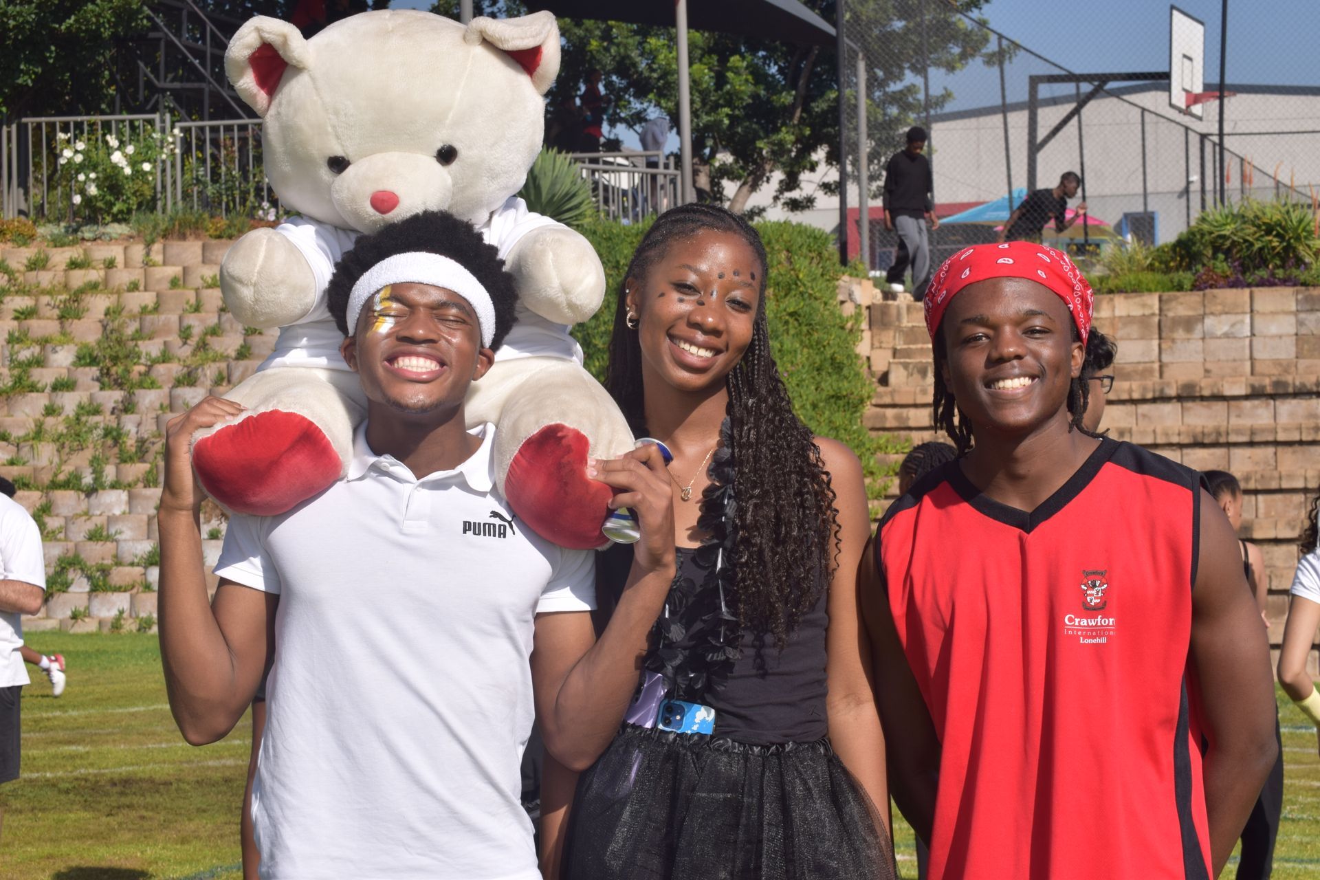 Three people smile for a photo outdoors, one holding a large teddy bear.