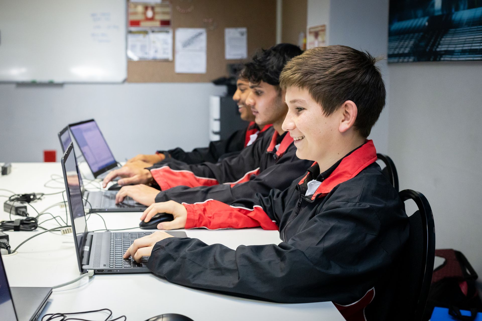 A group of young boys are sitting at a table using laptops.