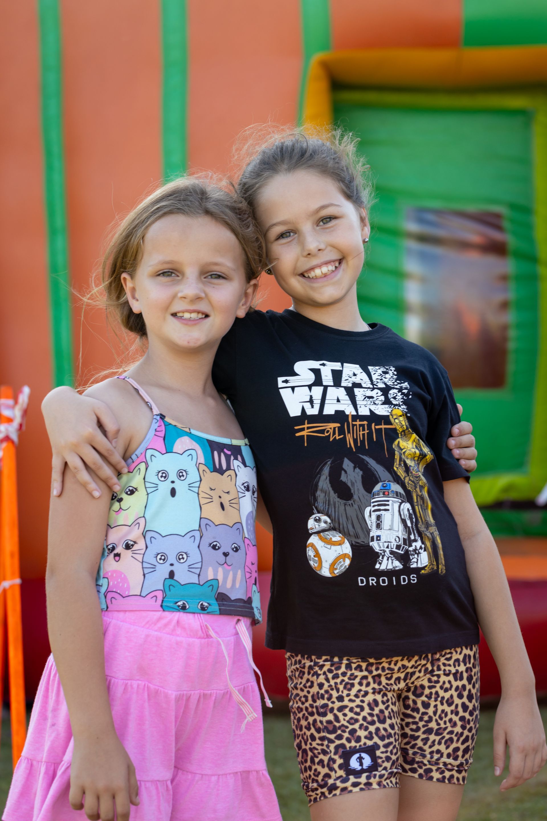 Two young girls are posing for a picture in front of a bouncy house.