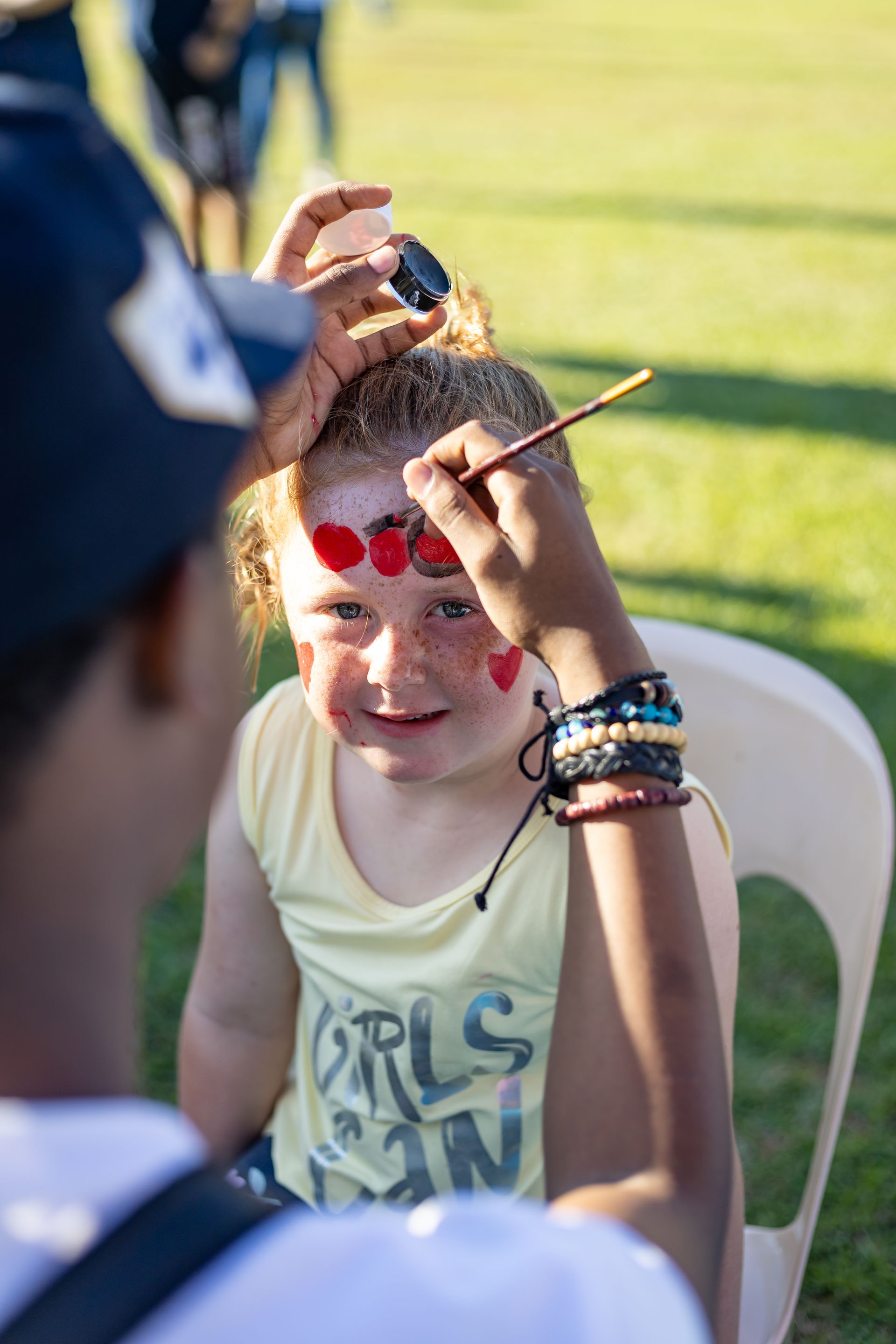 A little girl is getting her face painted by a man.