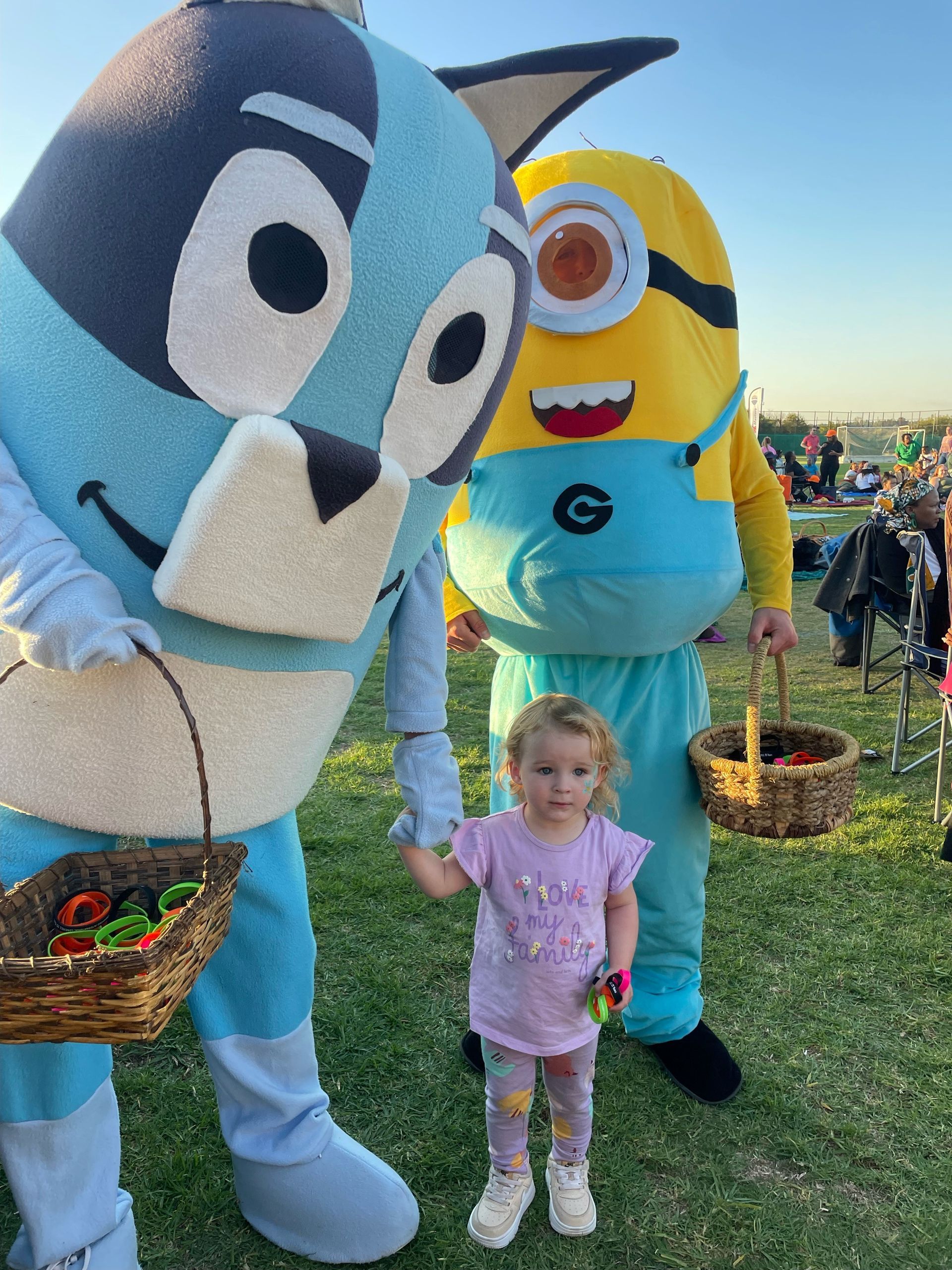 A little girl is holding hands with two mascots in costumes.