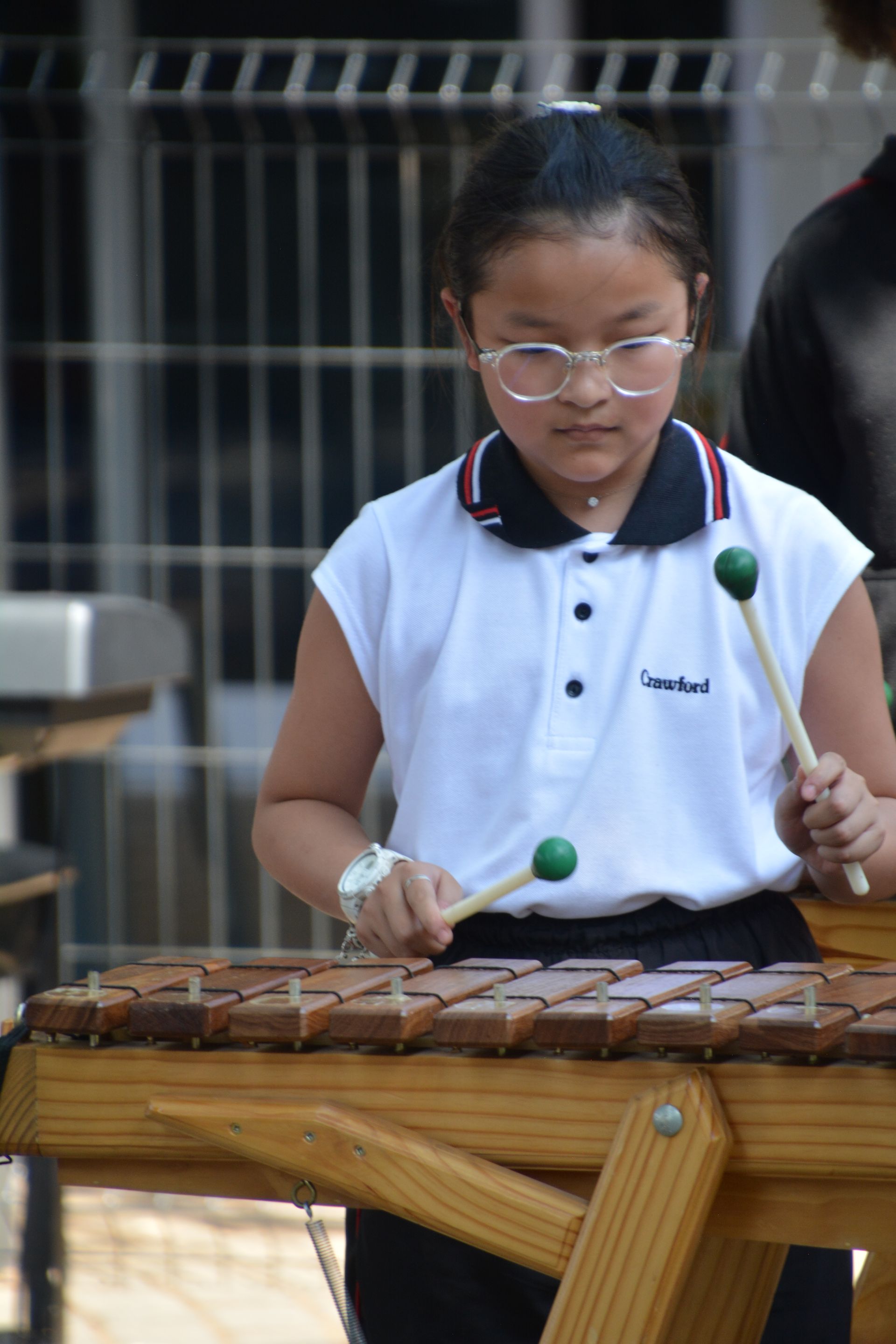 A young girl wearing glasses is playing a wooden xylophone.