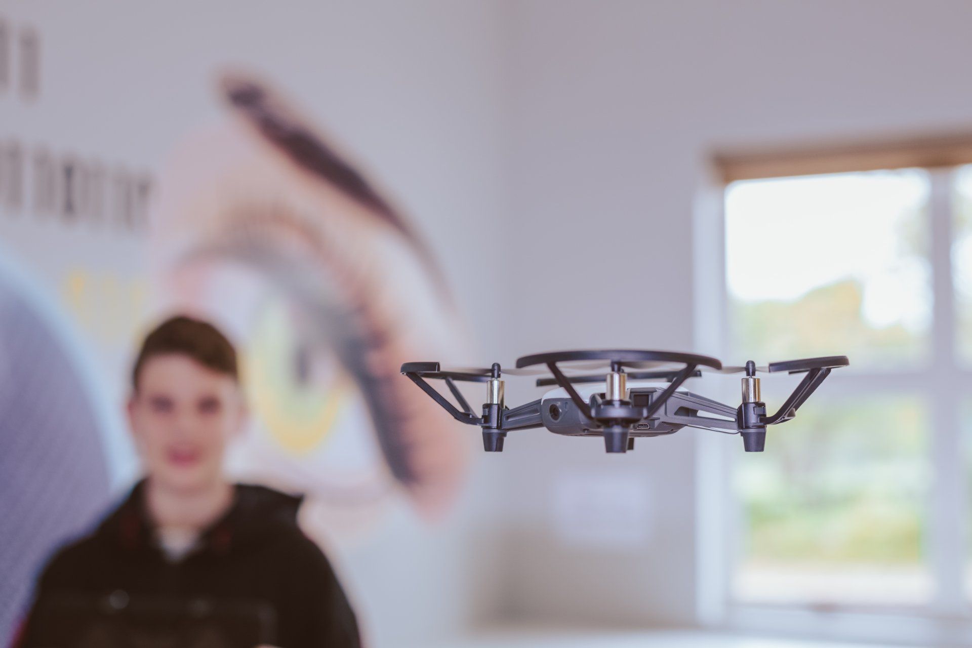 a boy is standing in front of a drone that is flying in the air .