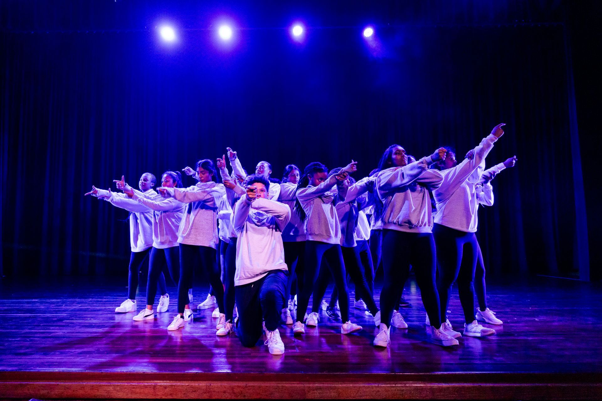 A group of people are dancing on a stage under purple lights.