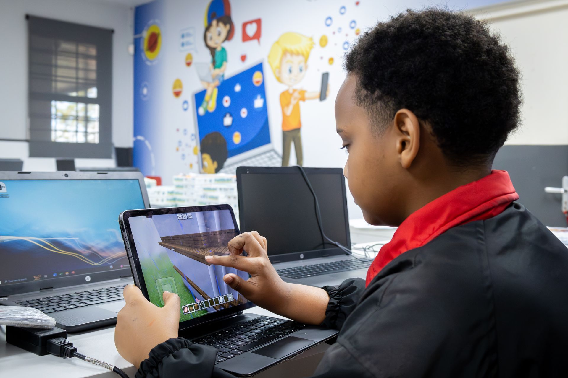 a little girl in a red and black jacket is looking at a tablet .