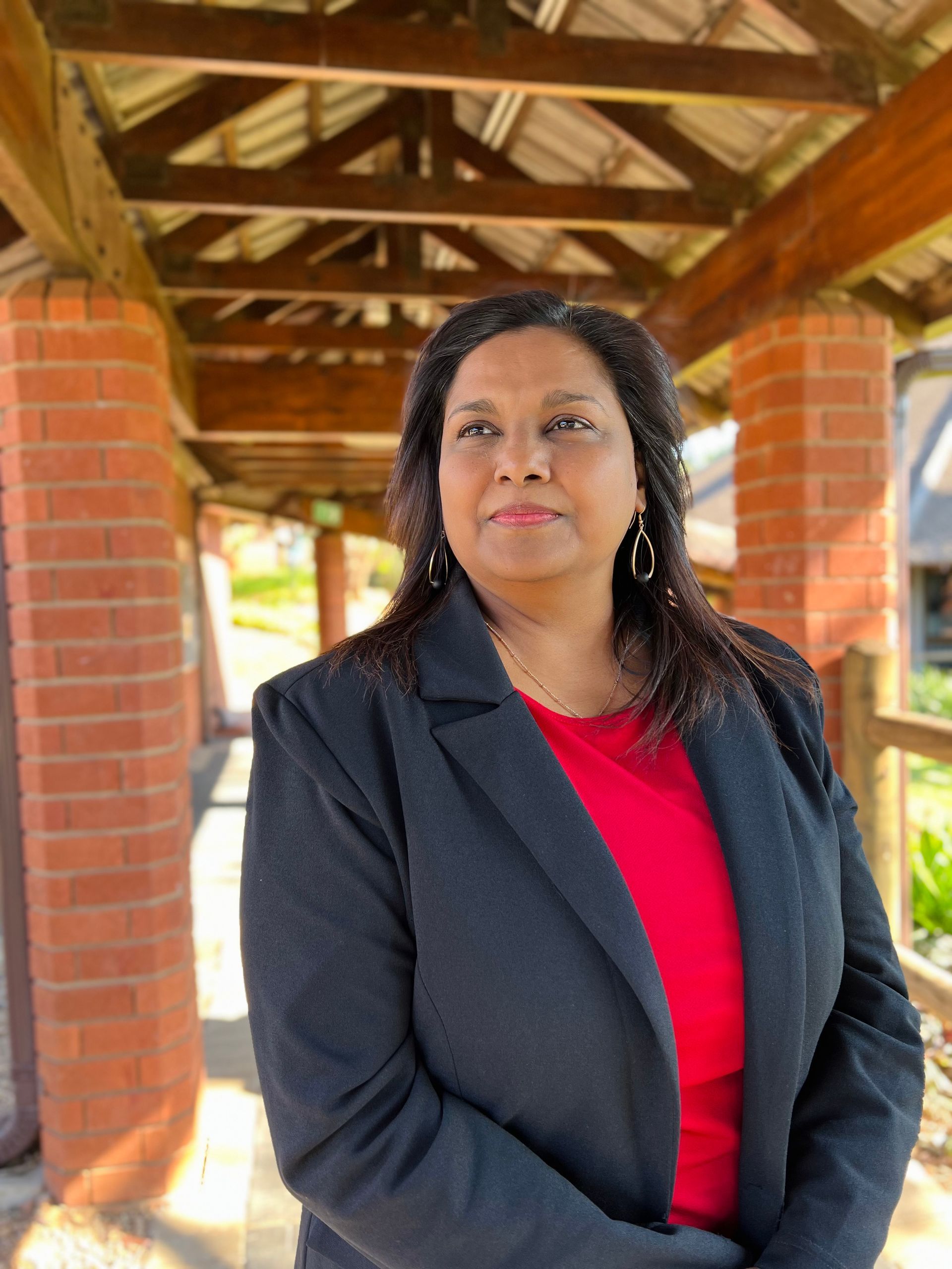 A woman in a black jacket and red shirt is standing under a canopy.