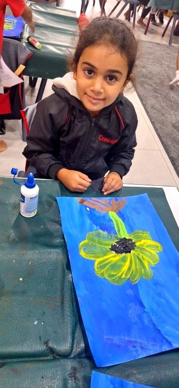 Young person smiling at the camera, holding a paintbrush while painting a sunflower.