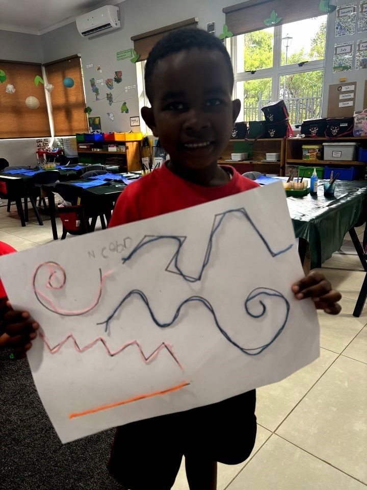 Boy holding artwork with lines and spirals, in a classroom.