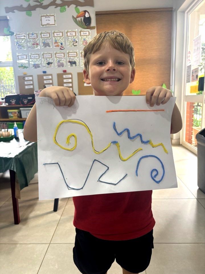 Smiling boy holding artwork with lines in different colors and shapes.