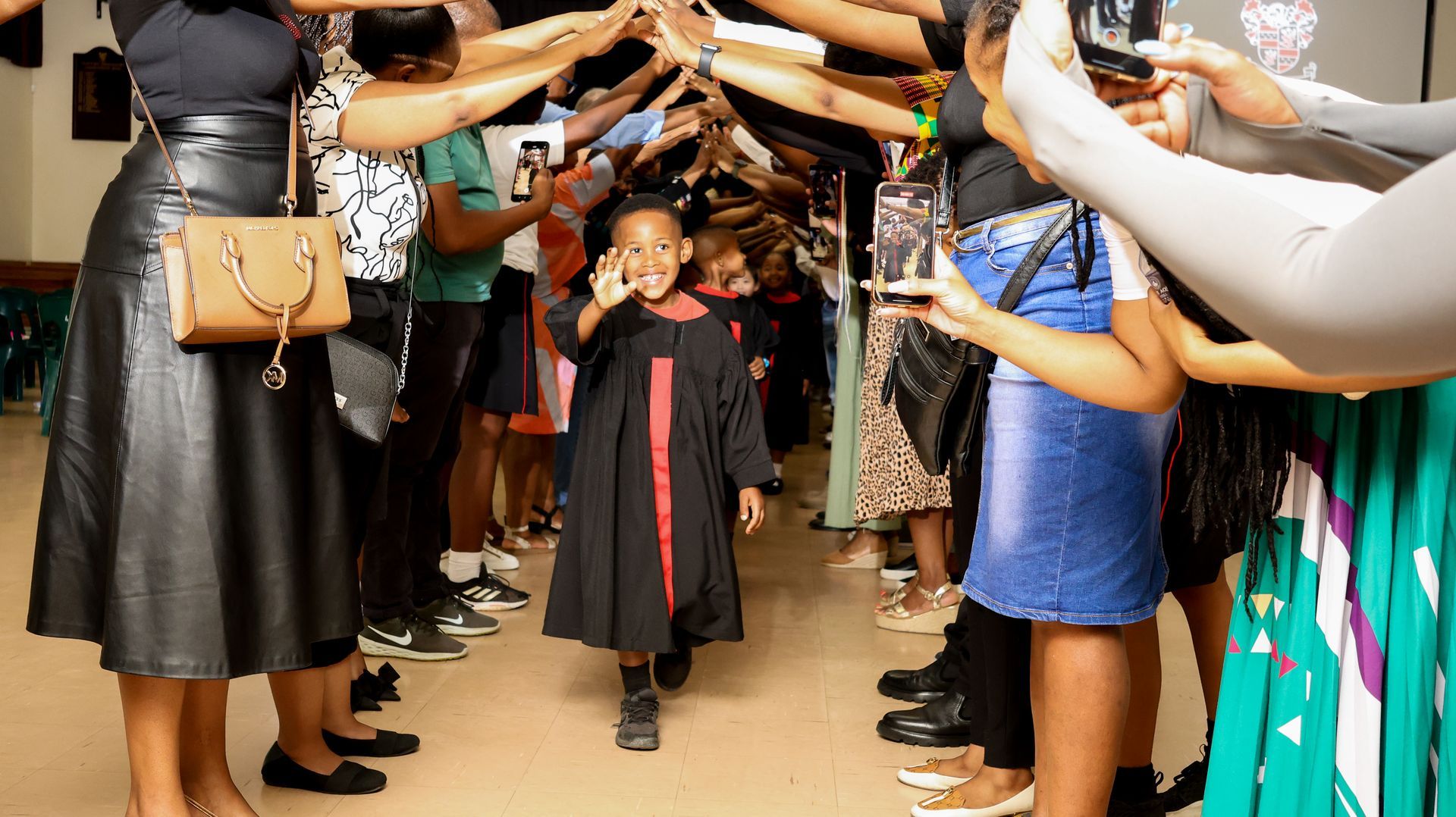 A little girl in a graduation gown is walking through a crowd of people.