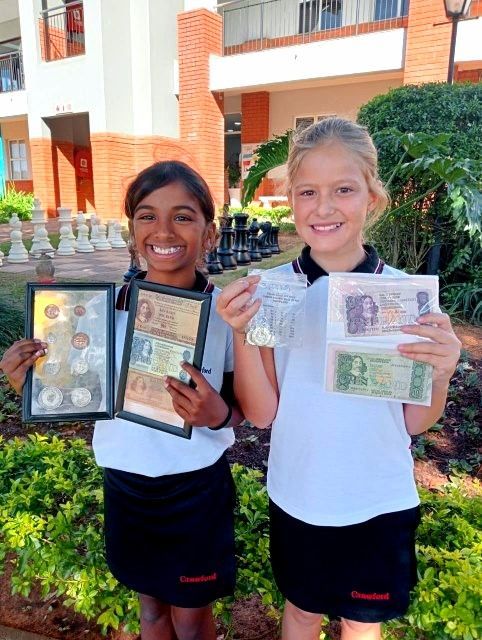 Two students holding and displaying old currency outdoors, smiling at the camera.