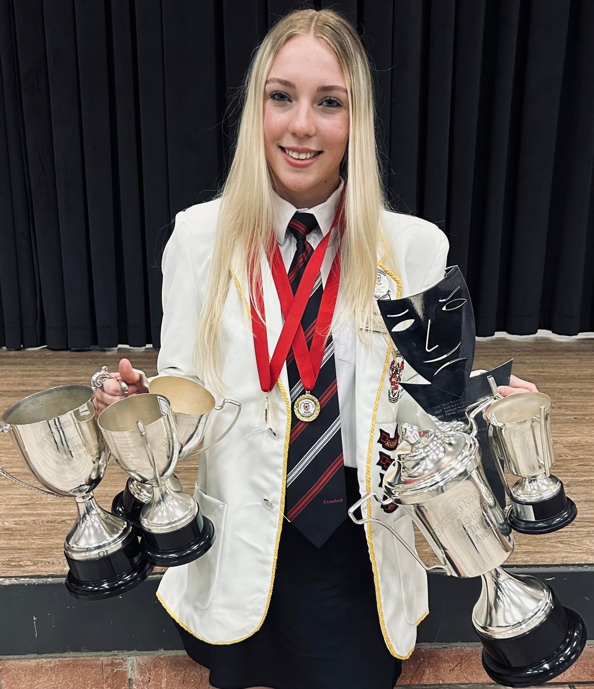 A woman in a suit and tie is kneeling down holding trophies.