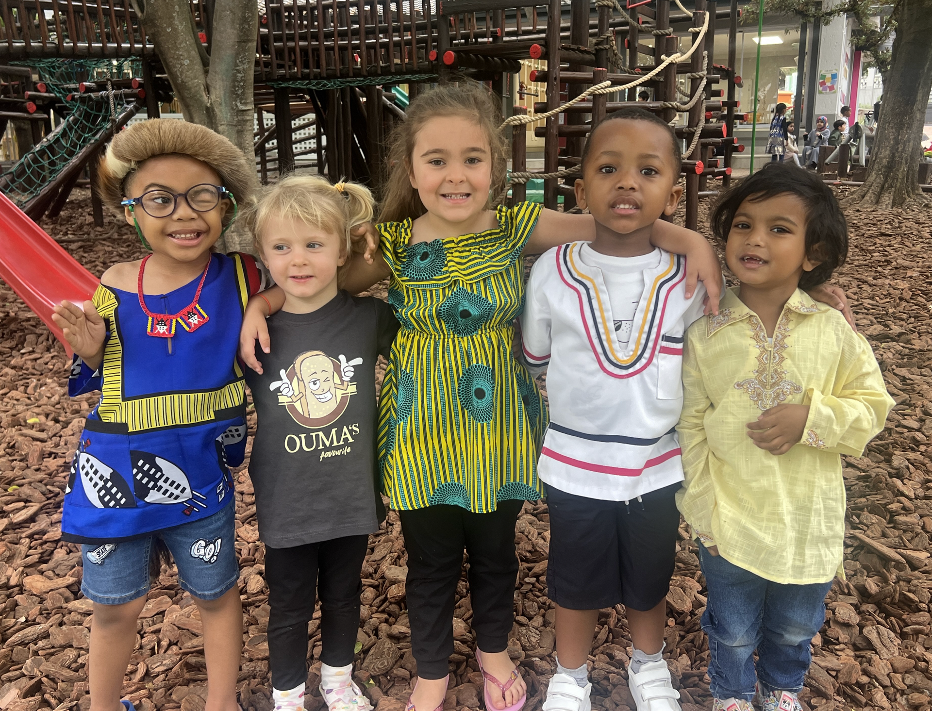A group of children are posing for a picture in front of a playground.