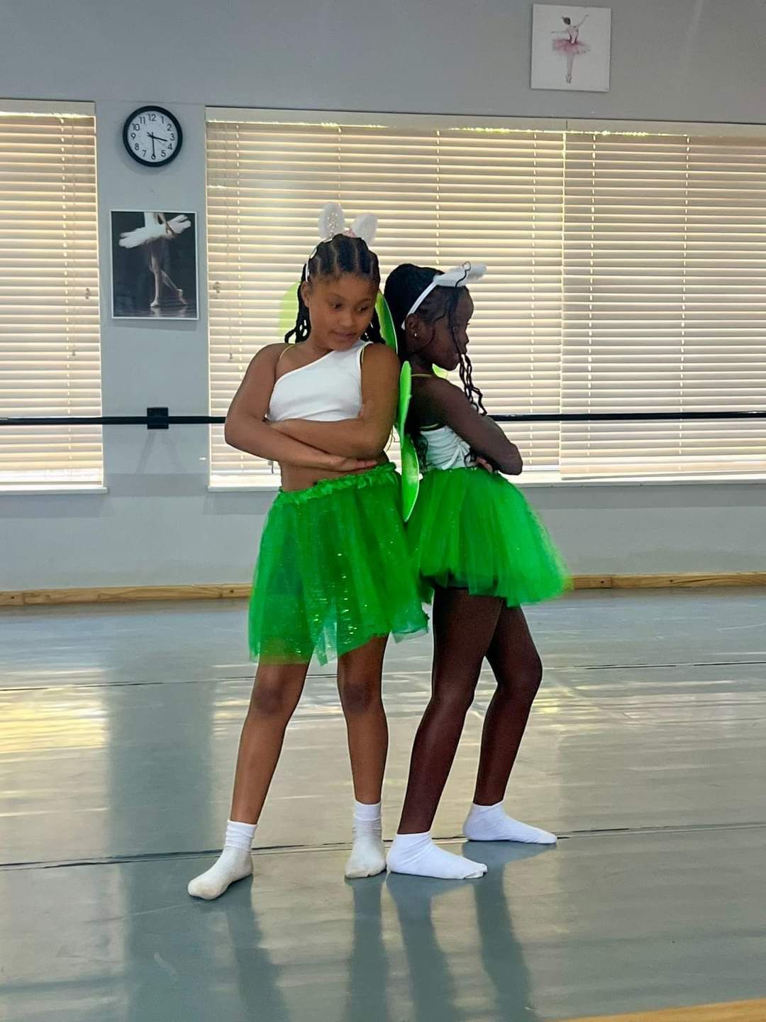 Two young girls in green tutus are dancing in a dance studio