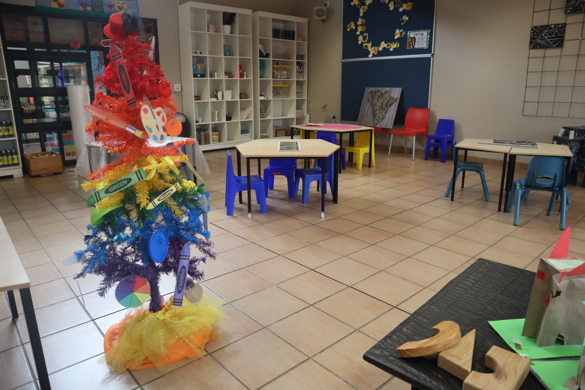 a classroom with tables and chairs and a rainbow colored christmas tree