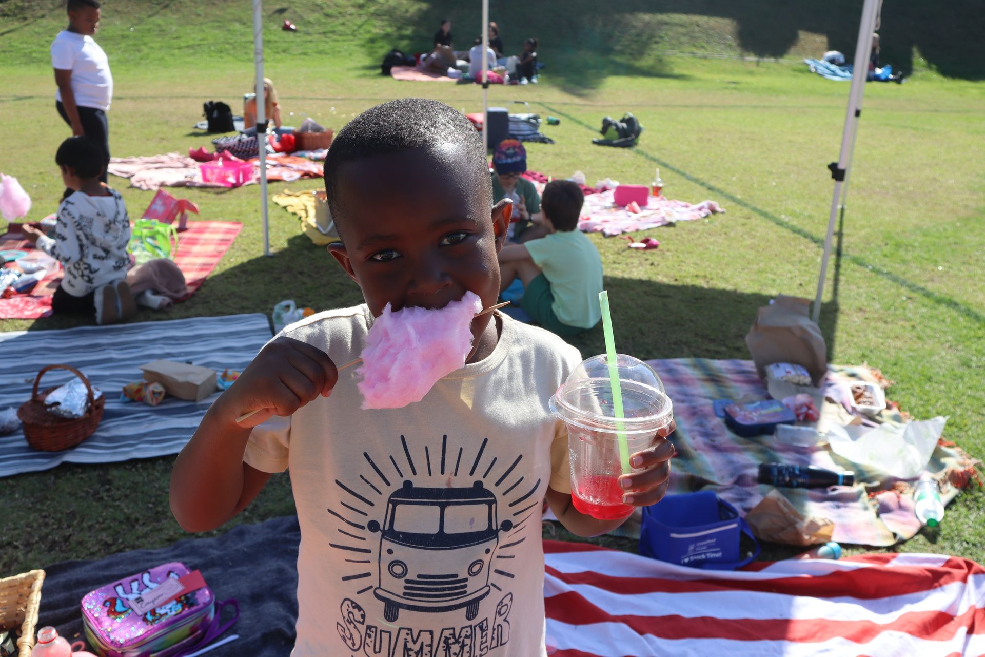 A young boy is eating cotton candy at a picnic in a park.