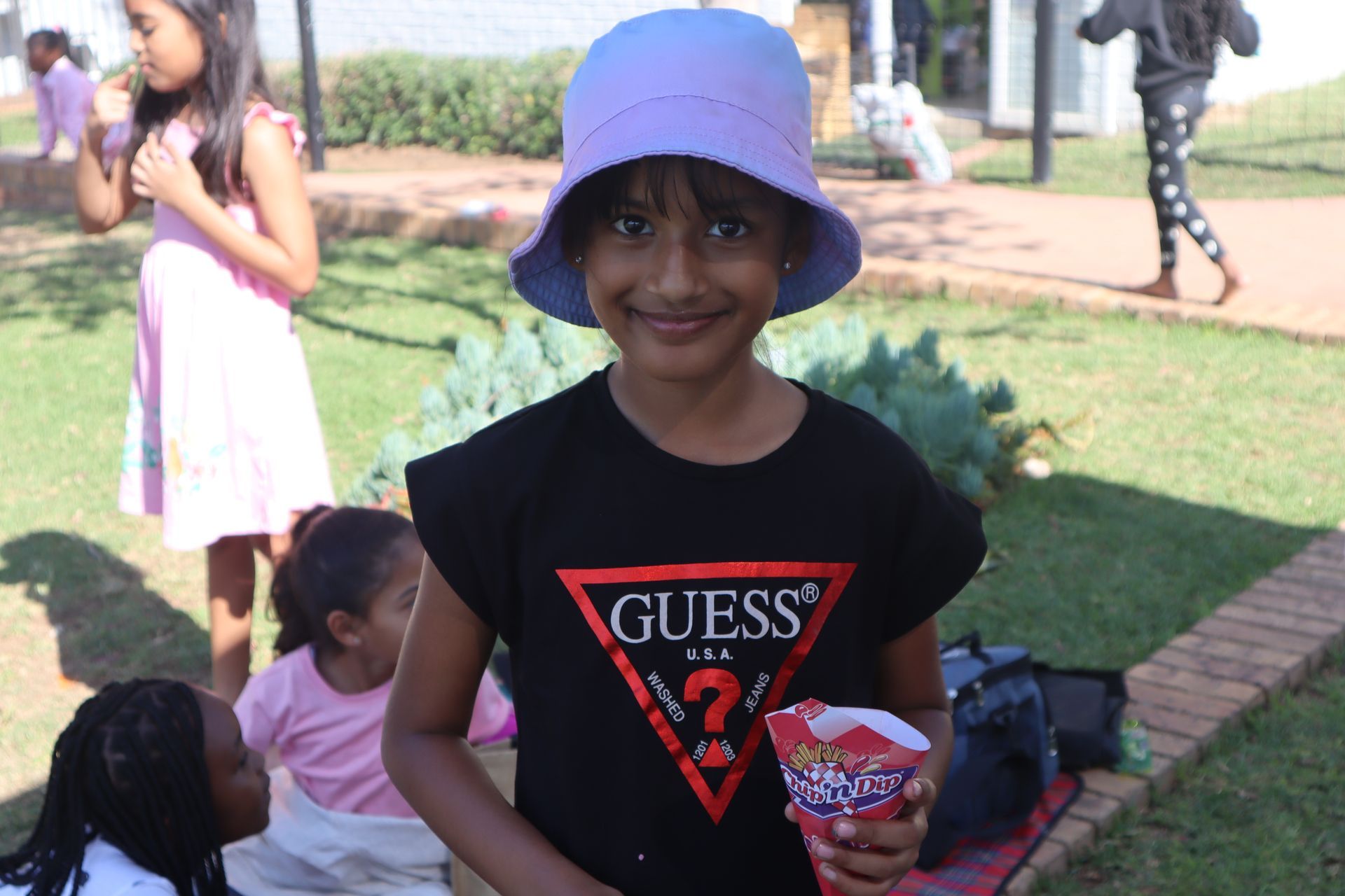 A little girl wearing a guess shirt and a hat