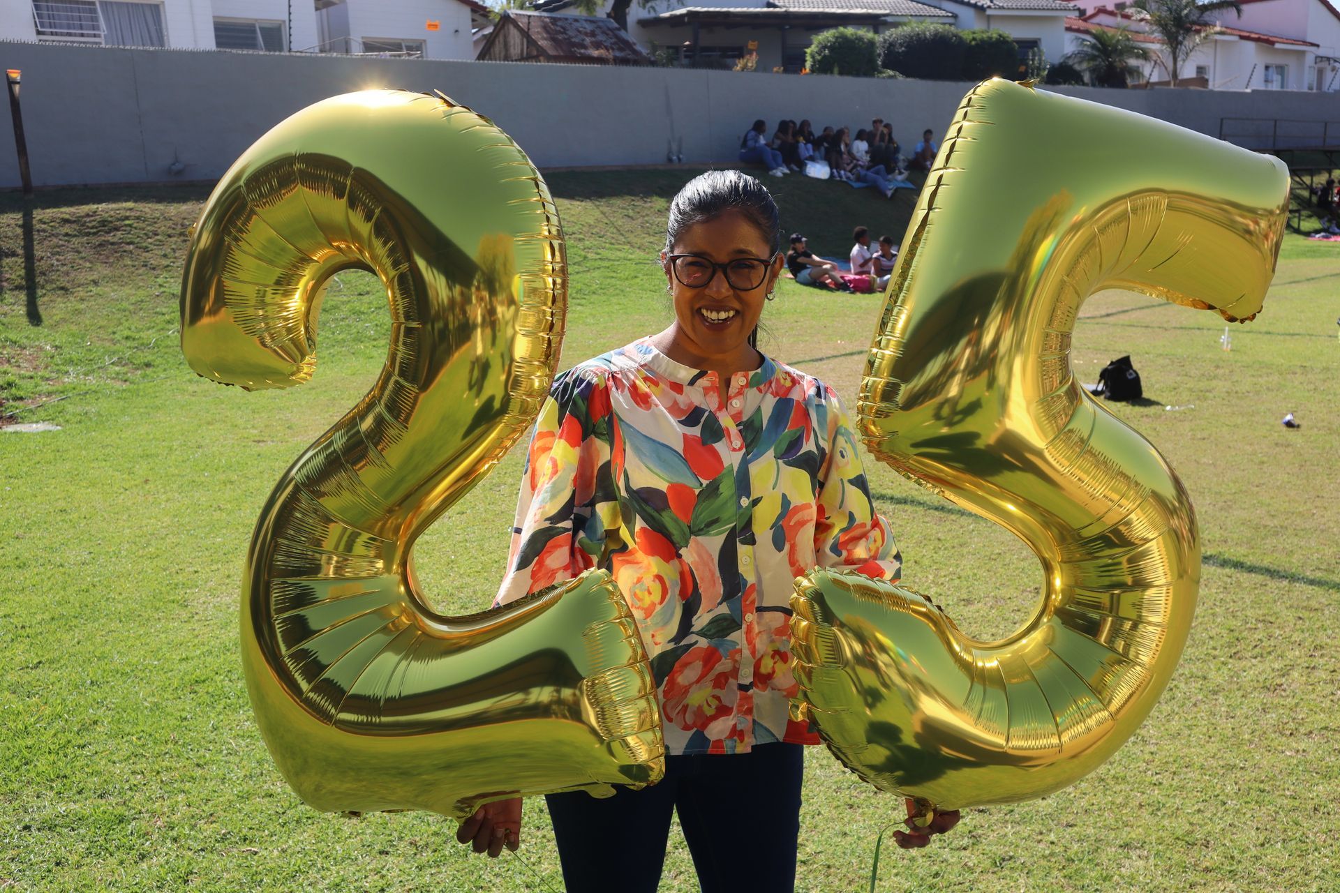 A woman is holding balloons in the shape of the number 25