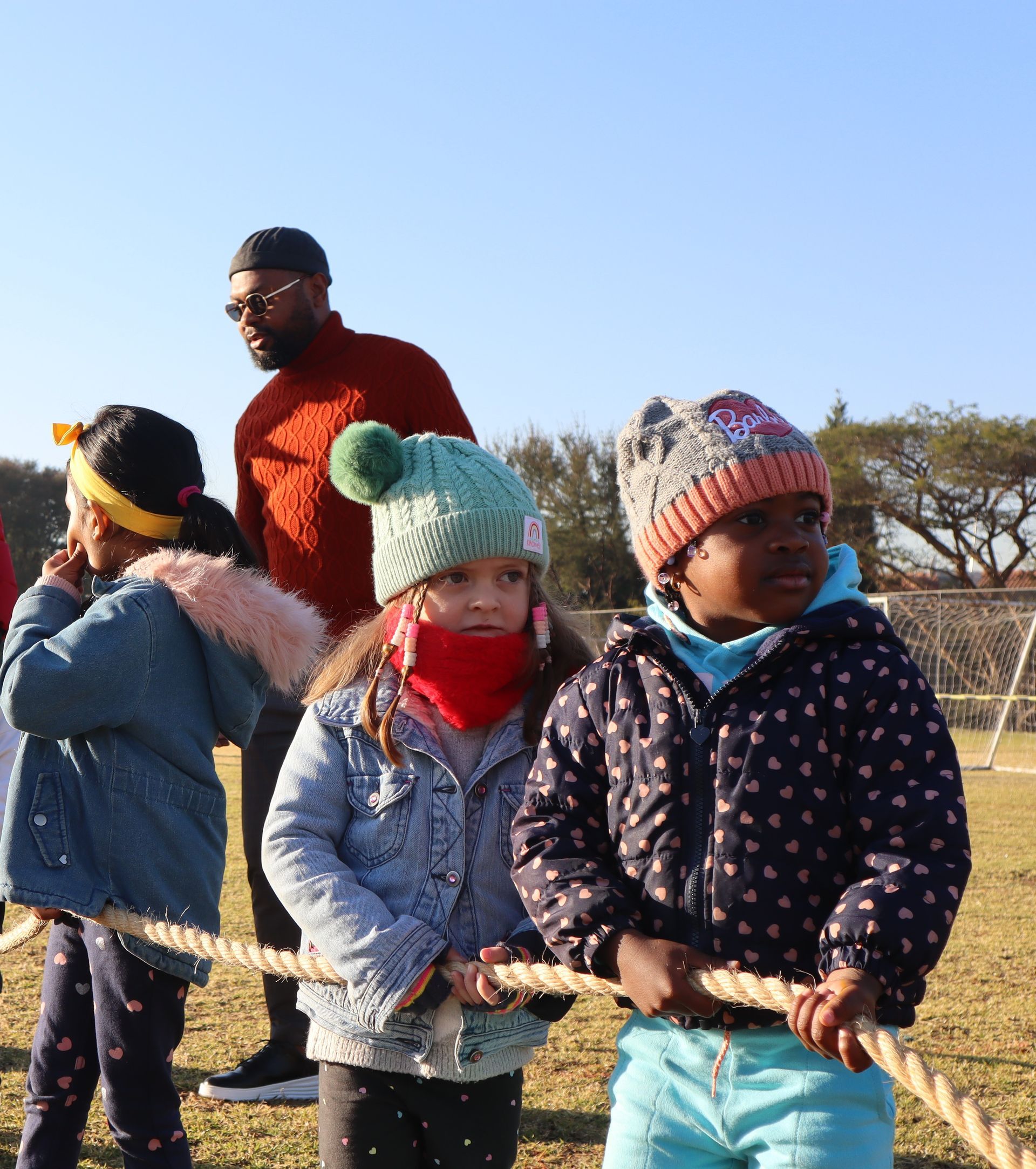 A group of young girls are pulling a rope in a field.